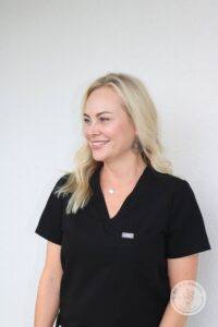 Blonde woman in black scrubs facing forward and looking to the left