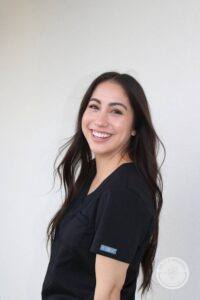 Woman with dark brown hair and black scrubs turned and smiling at camera
