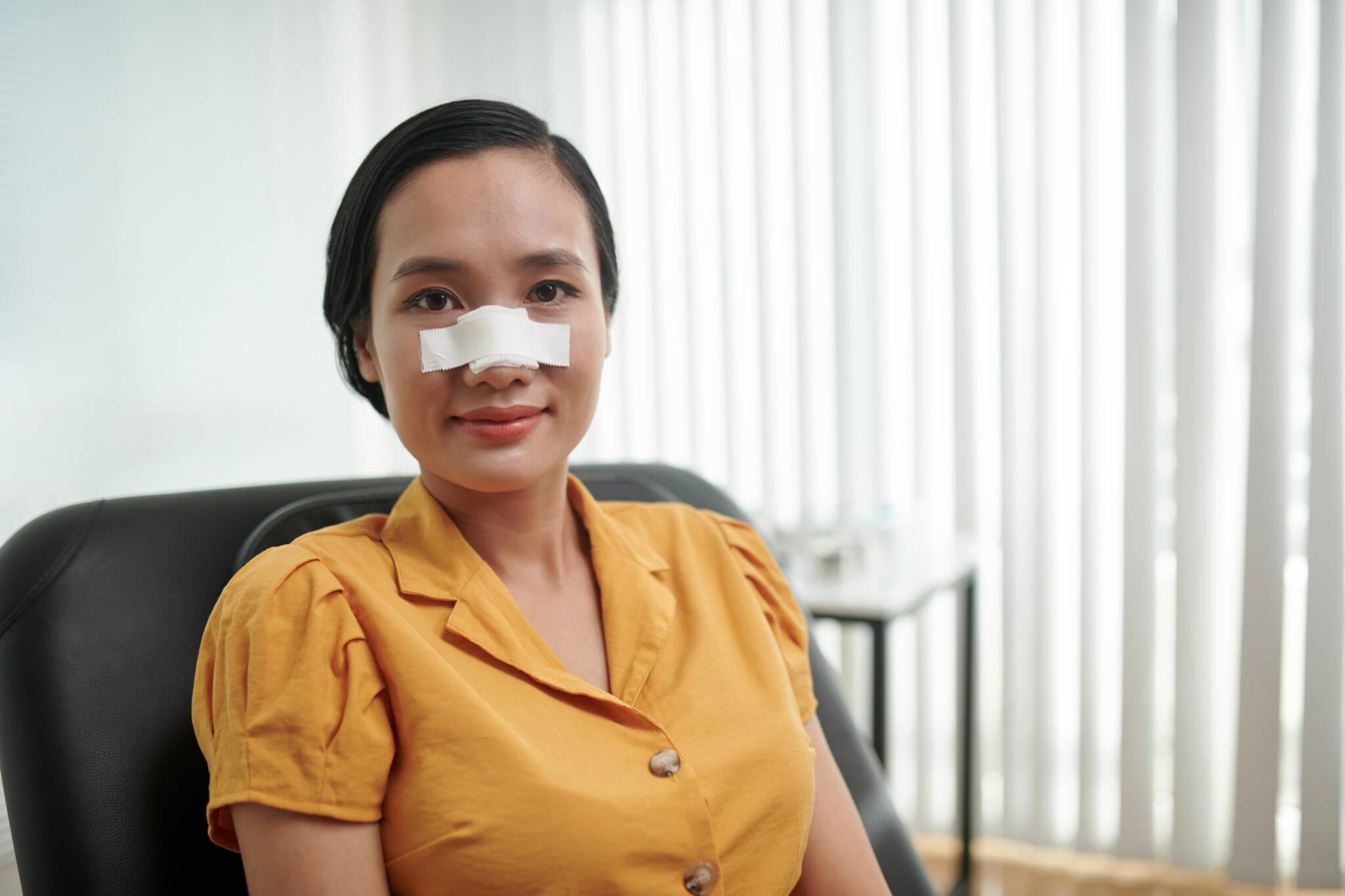 Young woman with bandage across bridge of nose following nose job