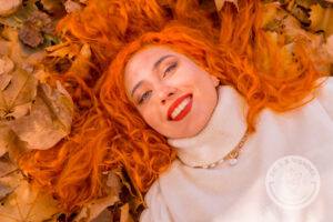 Red-haired girl lying on leaves in city park, fall season