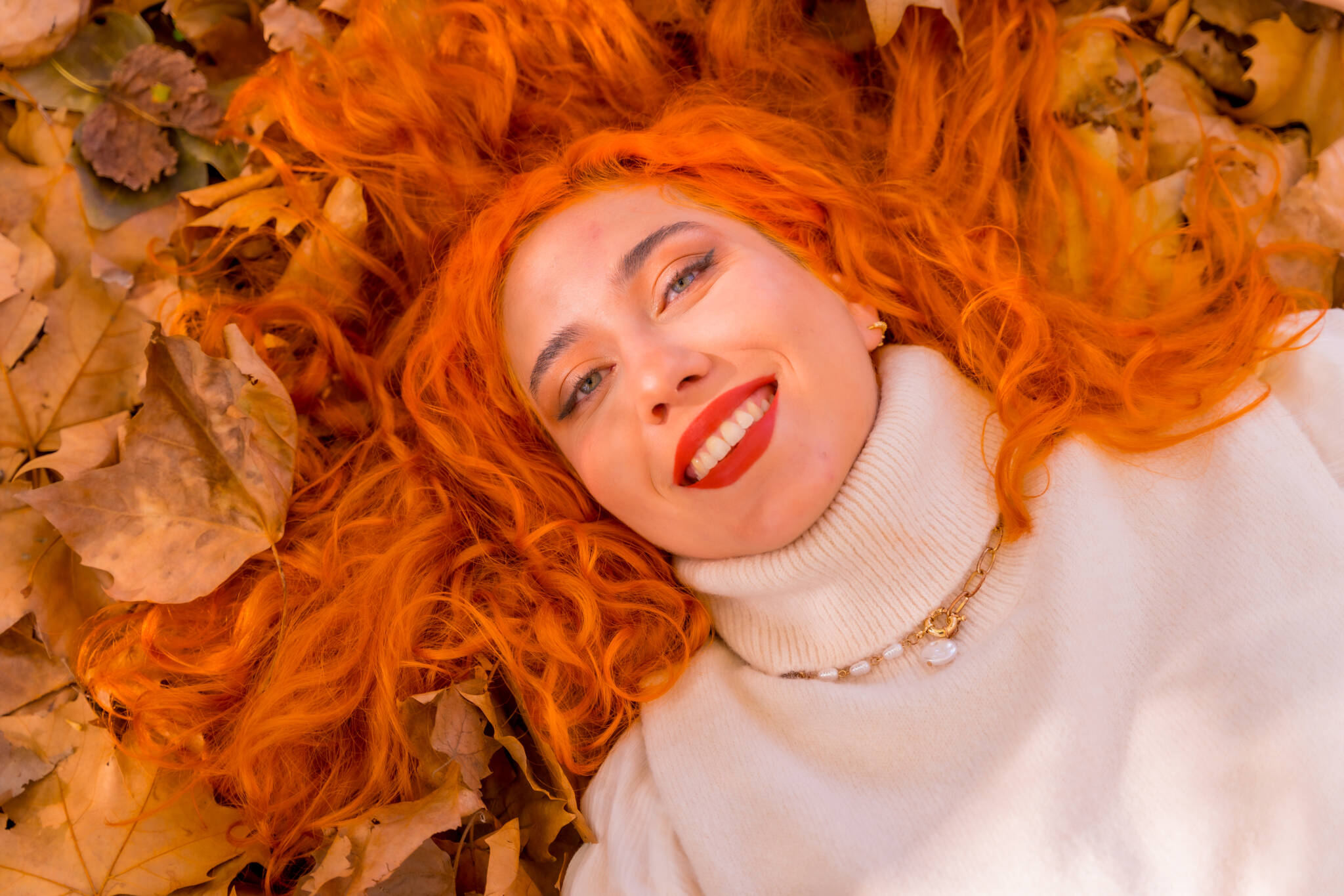 Red-haired girl lying on leaves in city park, fall season