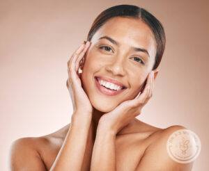 Brunette woman with a nose ring smiling while holding her face with both hands