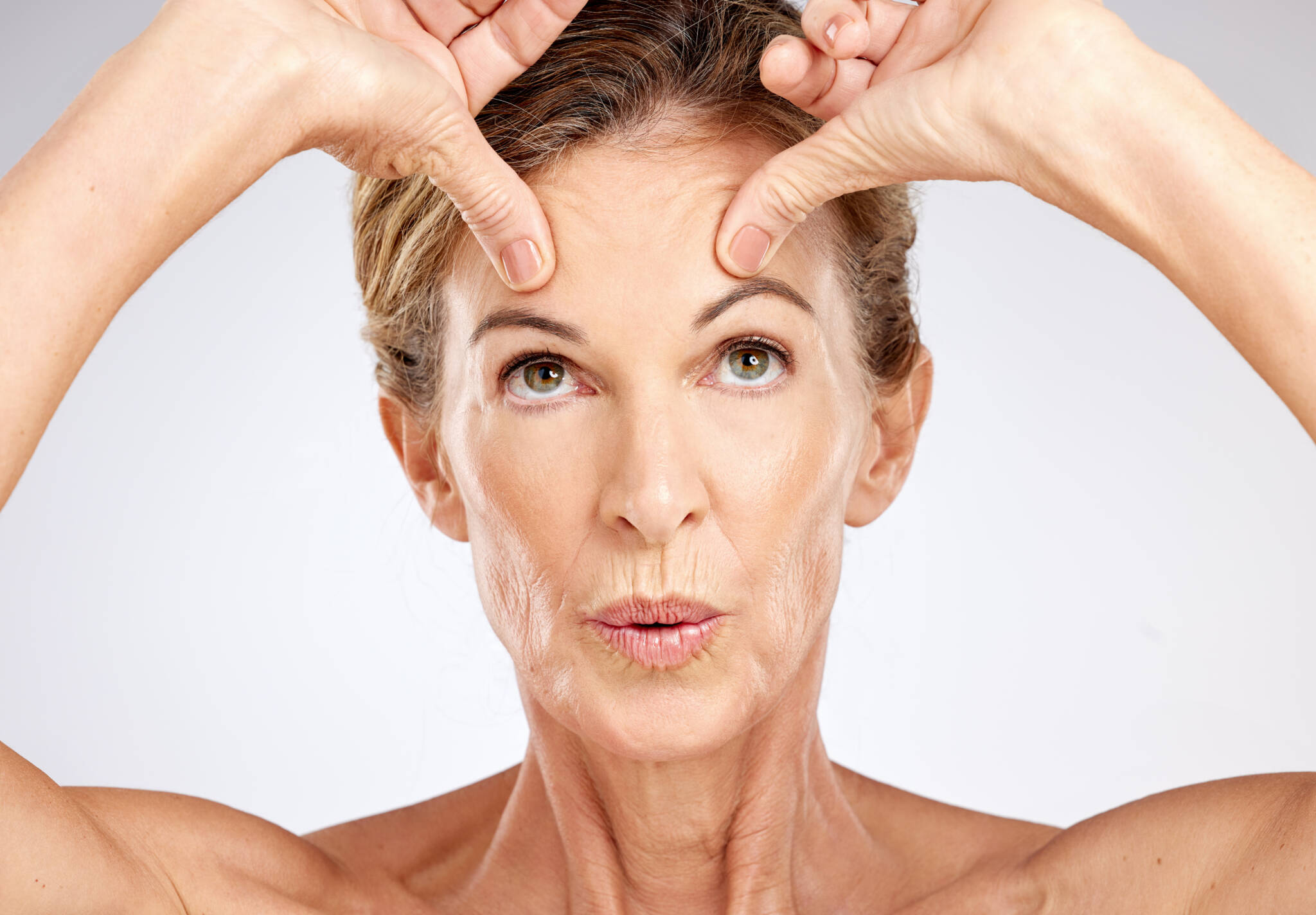 Portrait of senior woman using her thumbs to lift her brows and the skin on her forward upward