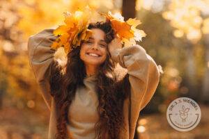 Brunette woman in brown sweater smiling while holding orange leaves against her head