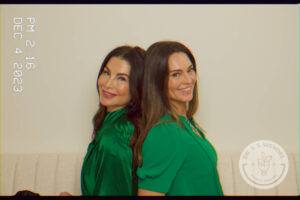 Lori Lankford & Paige Hastings smiling while wearing green tops with their backs against one another