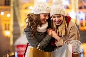 Two women wearing white beanies smiling while holding shopping bags