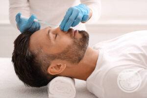 Brunette man undergoes non surgical rhinoplasty treatment from person wearing blue gloves