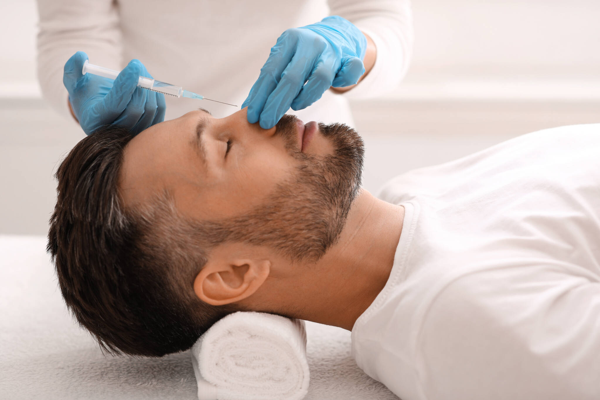 Brunette man undergoes non surgical rhinoplasty treatment from person wearing blue gloves