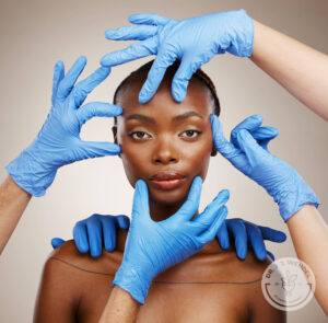 Six hands in blue gloves touching and pulling black woman's face