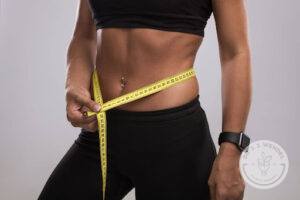 woman wearing black sports bra and leggings measures abdomen with measuring tape