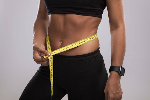 woman wearing black sports bra and leggings measures abdomen with measuring tape