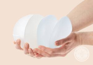 Female hands holding stack of different types of breast implants.