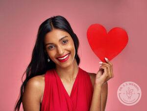 Indian woman with long black hair smiling while holding a red heart