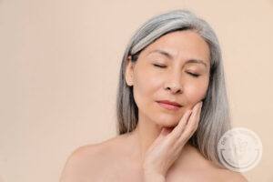 Older woman with beautiful skin and long grey hair caressing her face with her eyes closed