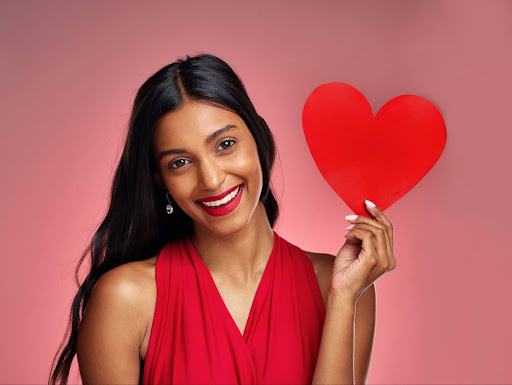 Indian woman with long black hair smiling while holding a red heart