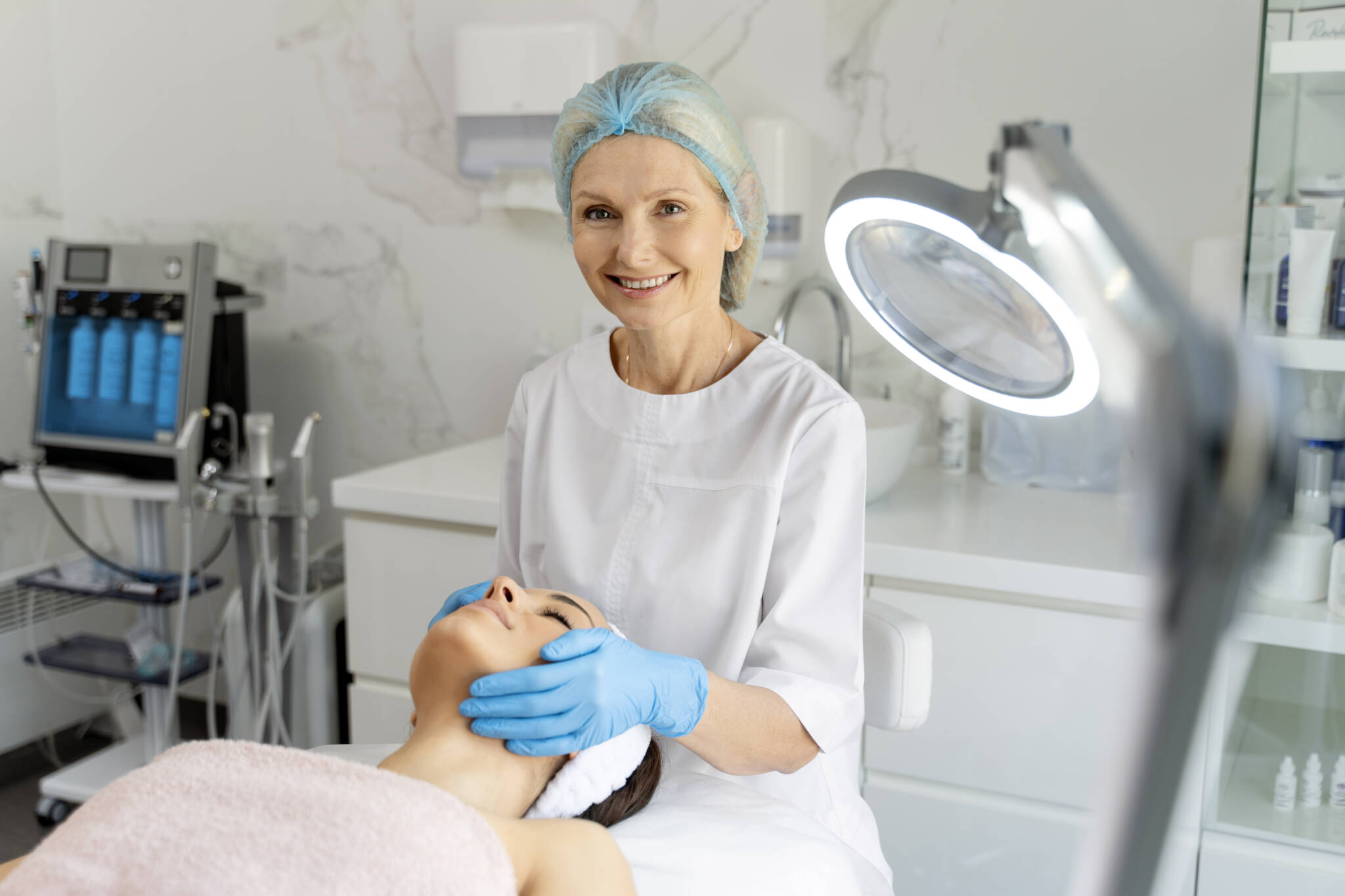 Woman laying on patient table while a female practitioner performs facial treatment