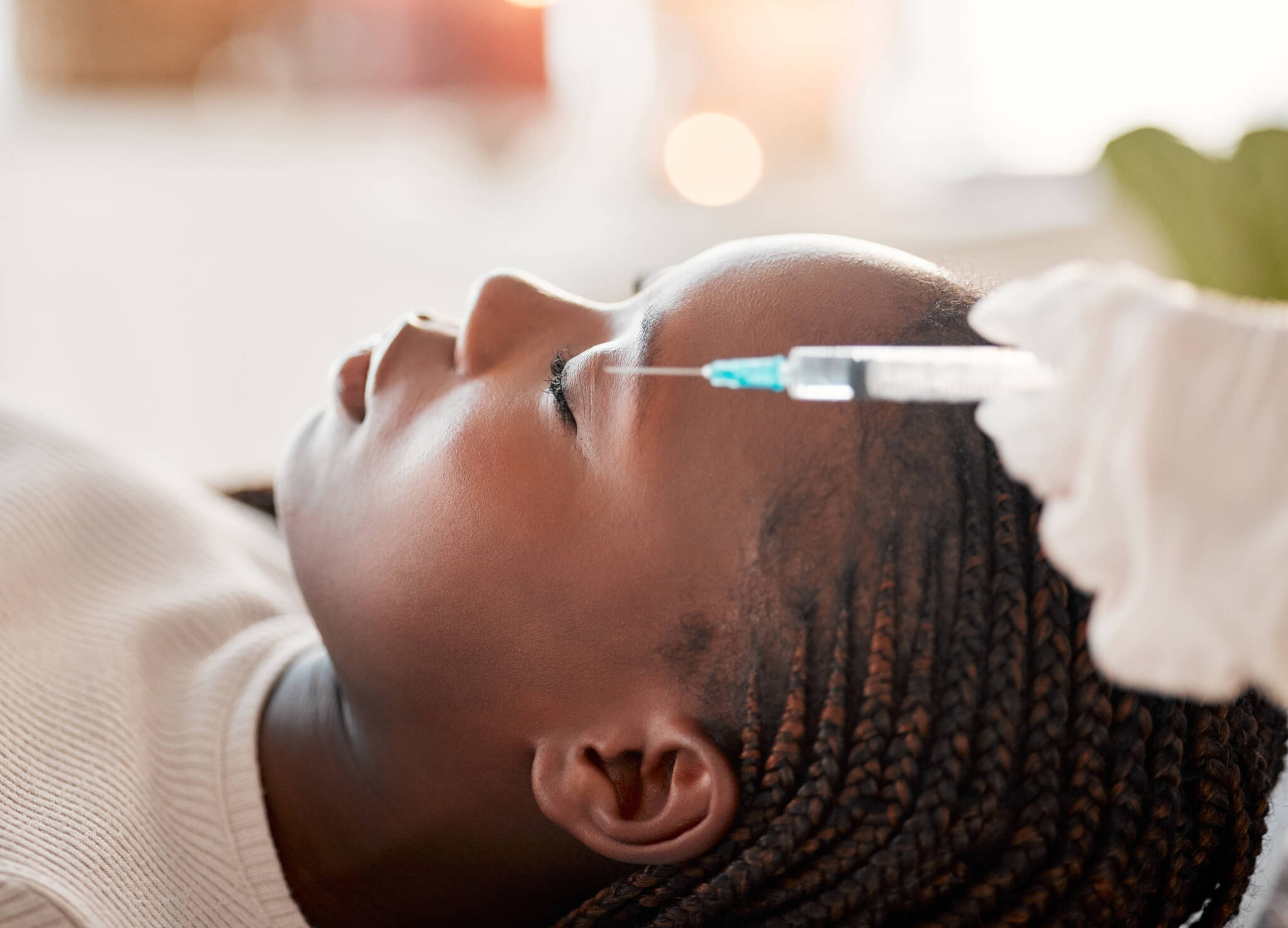Black woman laying down with her eyes closed while receiving facial injections