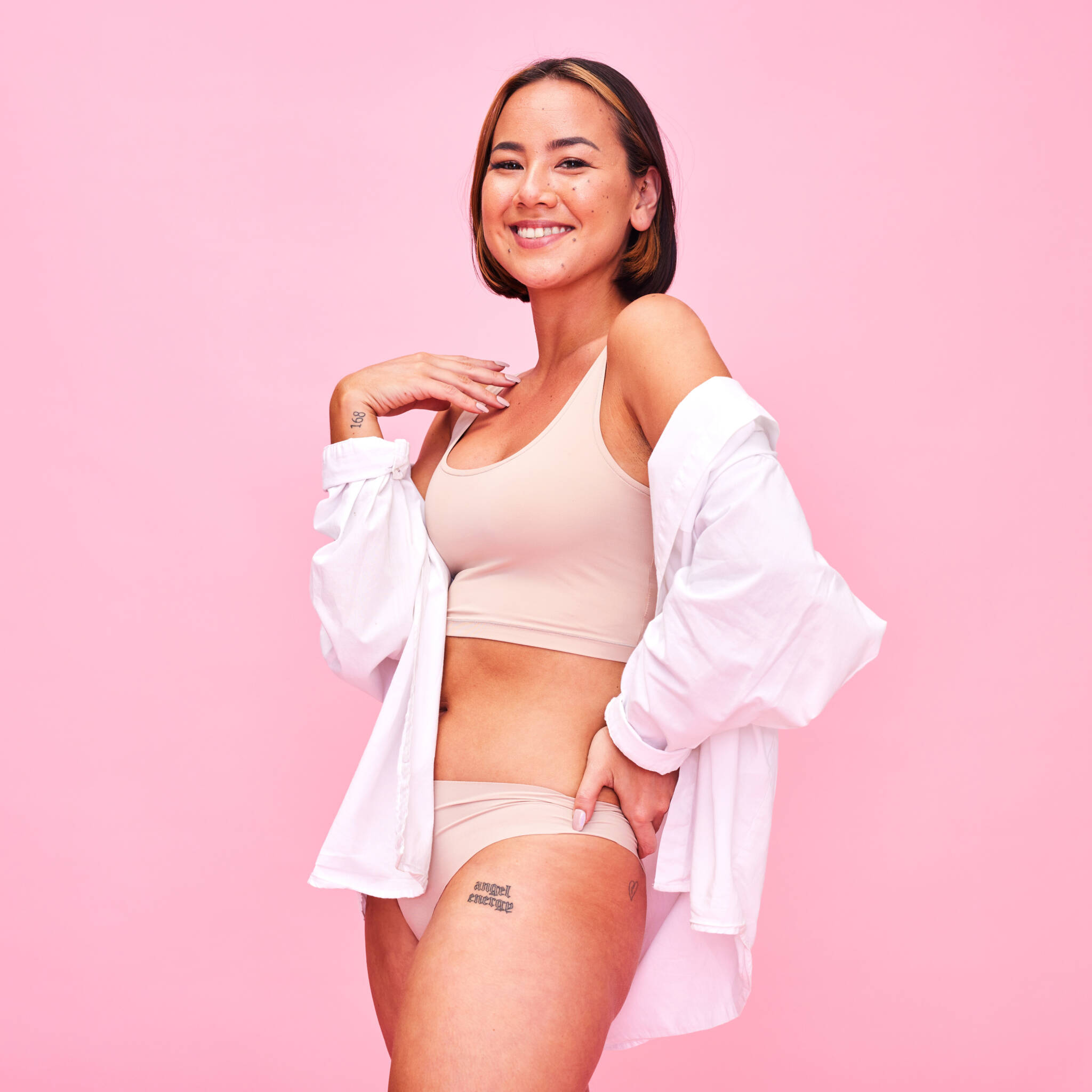 Asian woman wearing underwear and an open white button down in front of a pink backdrop