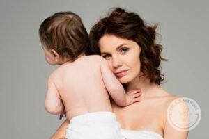 A mother holds her child while considering if a mommy makeover procedure is right for her.