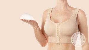 Woman holds breast implant while modeling a breast augmentation surgery bra.