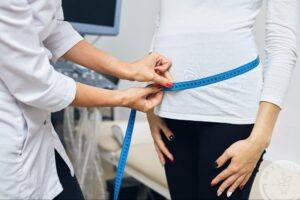 Doctor measuring woman's waist before weight loss procedure, concept of fat banking and body contouring