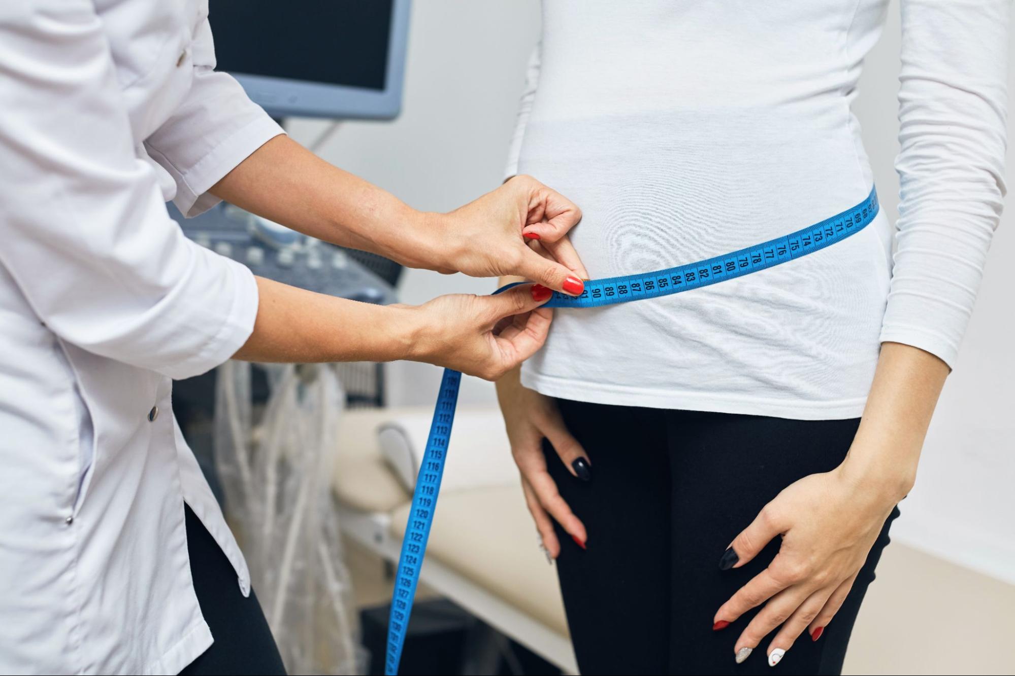 Doctor measuring woman's waist before weight loss procedure, concept of fat banking and body contouring