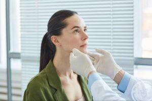 Plastic surgeon evaluating a woman's chin and facial profile during a chin implant consultation.